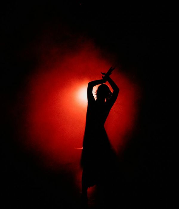 Person in a dynamic yet graceful pose in a minimalist dark room.