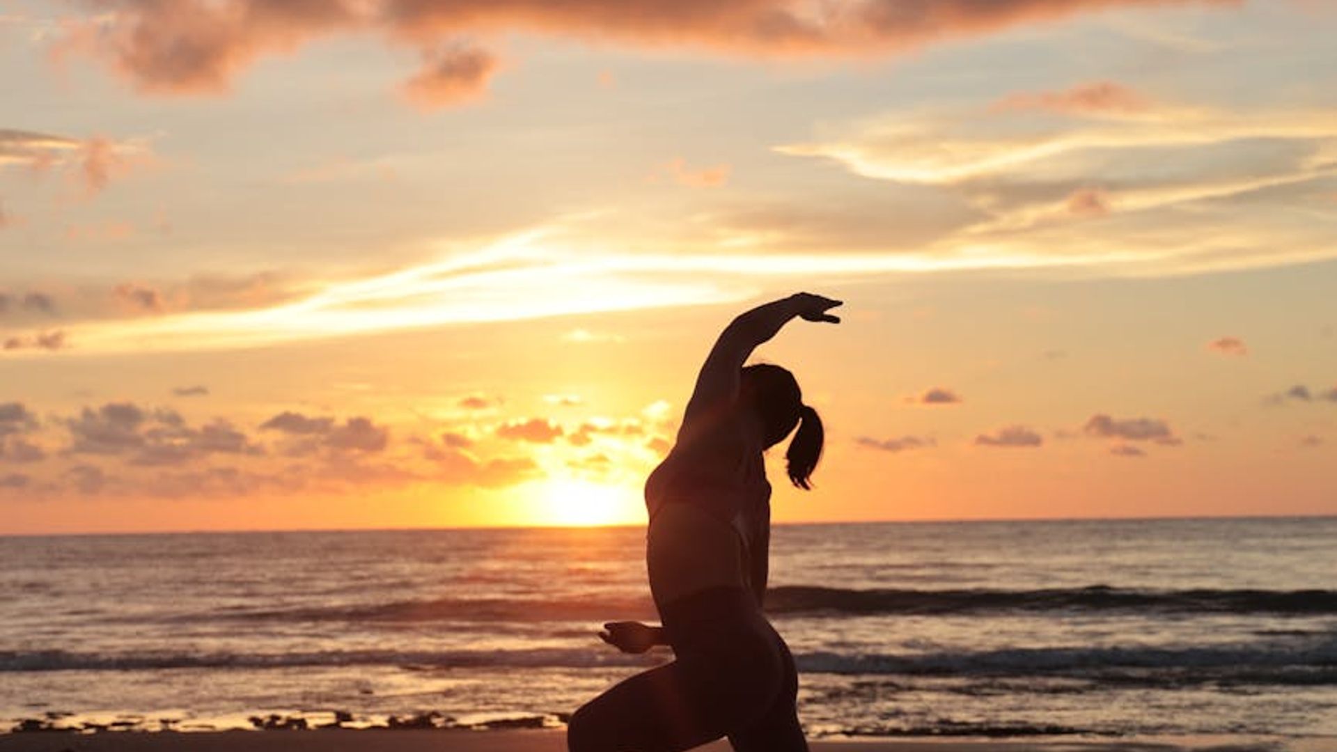 Silhouette of a person stretching at sunrise with pink and green tones.